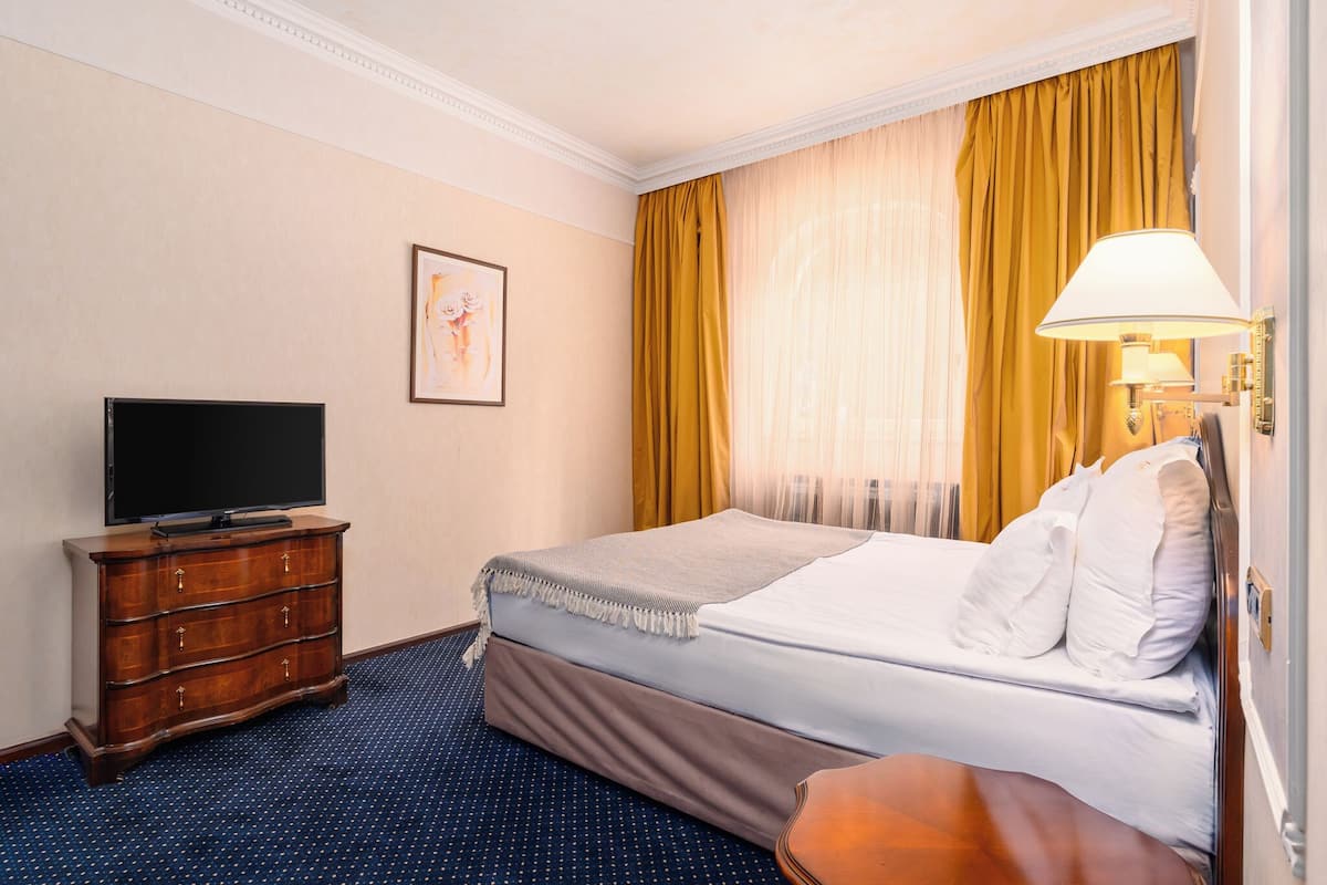 A hotel room with a bed, a dresser, a television, a lamp, and a painting on the wall.