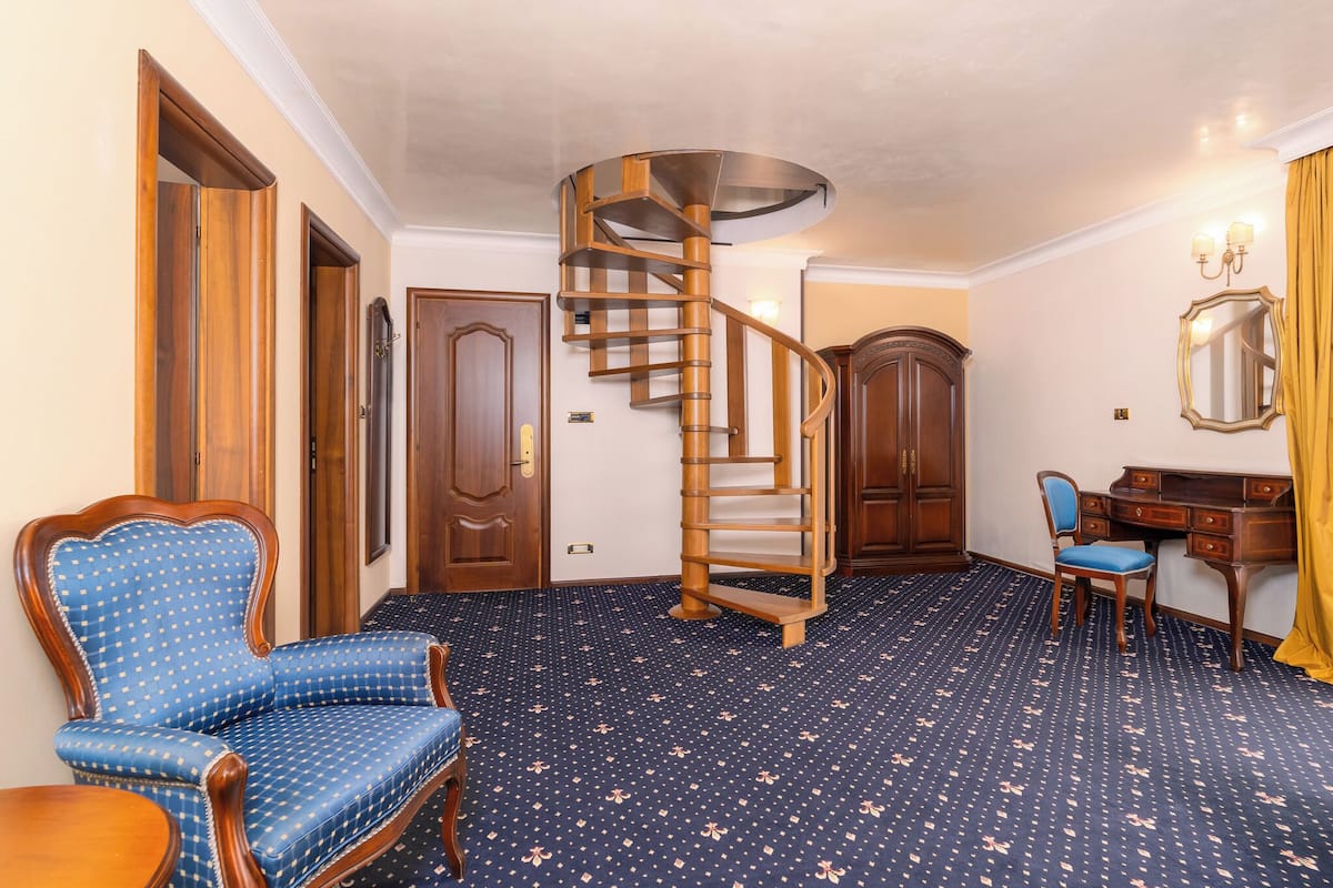 A room with a spiral staircase, wooden furniture, a desk, and a patterned carpet.
