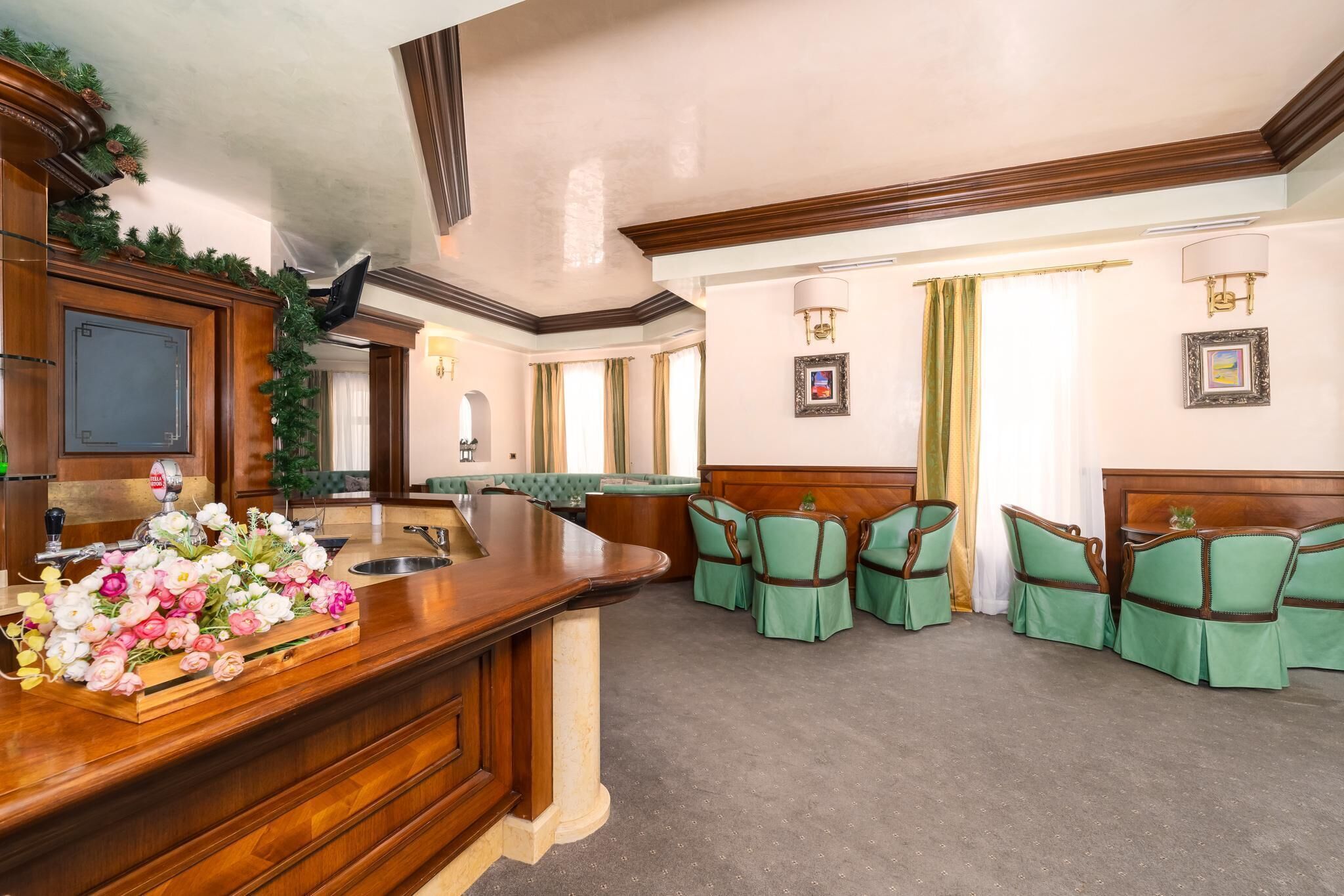 Un vestíbulo de hotel con mostrador de recepción, sillones tapizados en verde, zona de recepción de madera y cuadros en las paredes.
