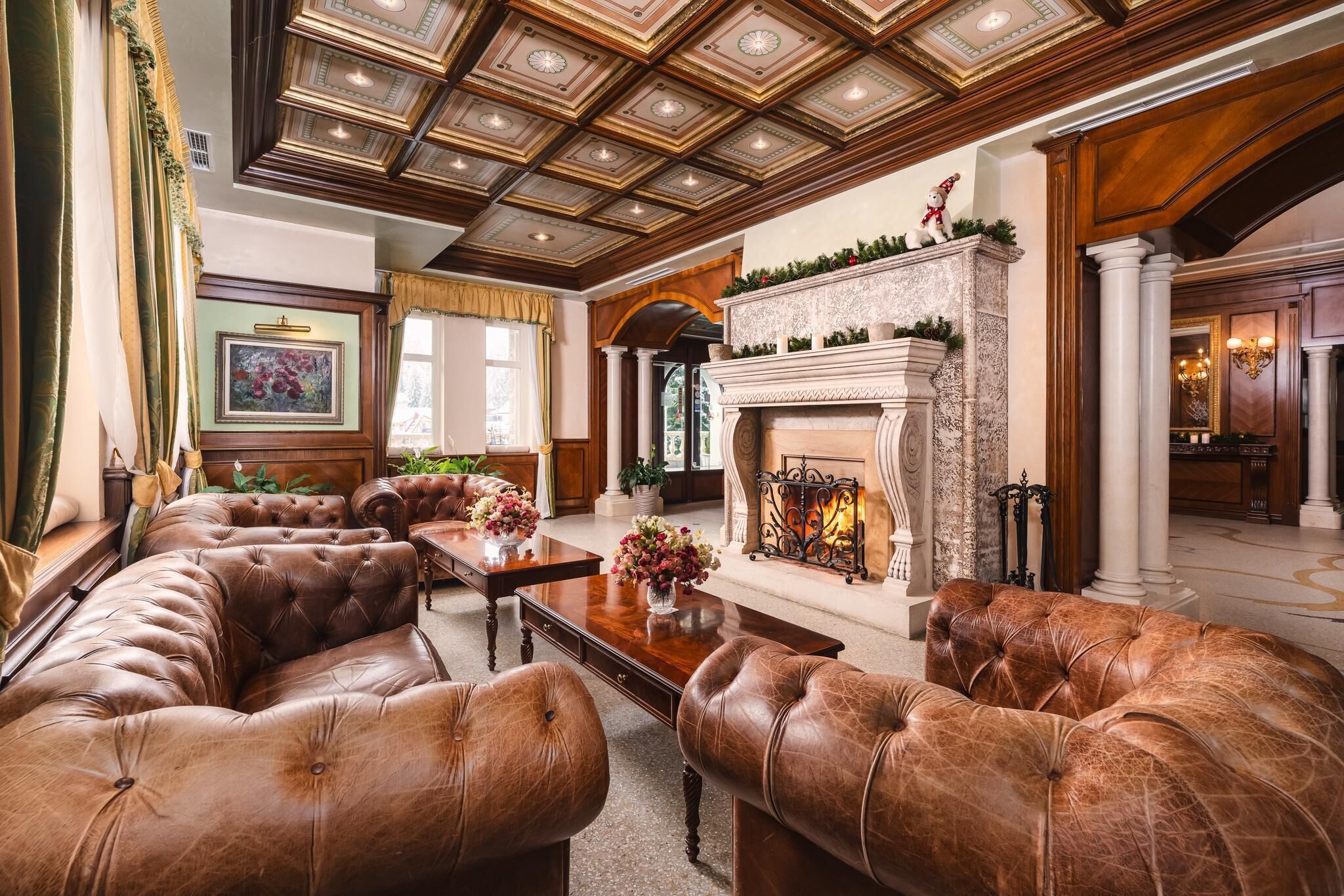 Ein luxuriöses Wohnzimmer mit Ledersofas, einem Kamin und einer hohen Decke mit aufwendigen Holzschnitzereien.