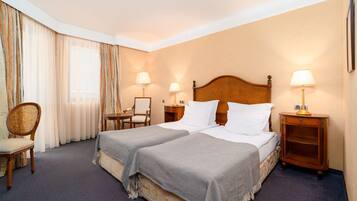A hotel room with a double bed, two bedside tables with lamps, a chair, and a window with curtains.