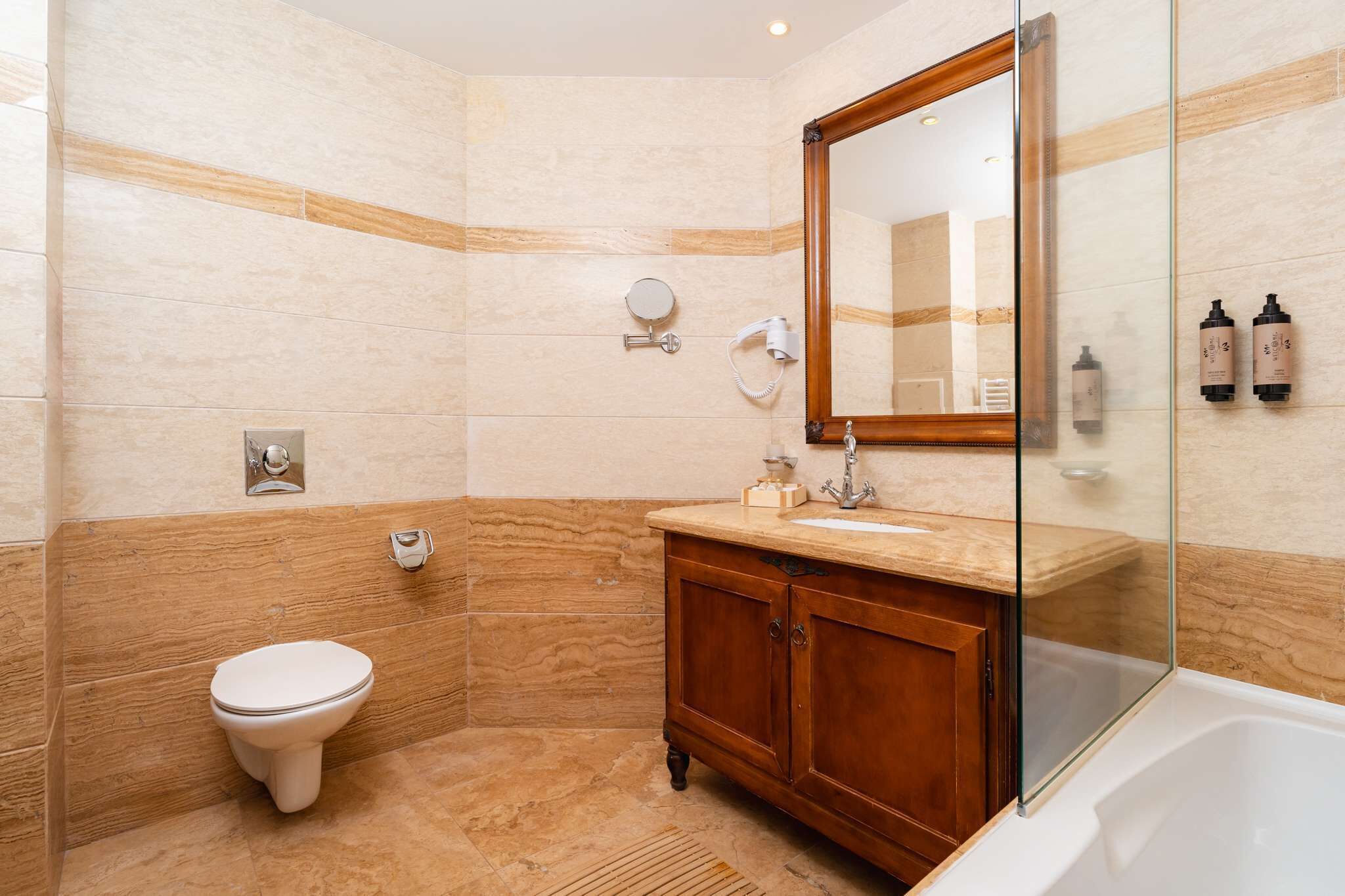 Et moderne badeværelse med en marmorvæg, et trækommode, en glas brusekabine og et toilet.