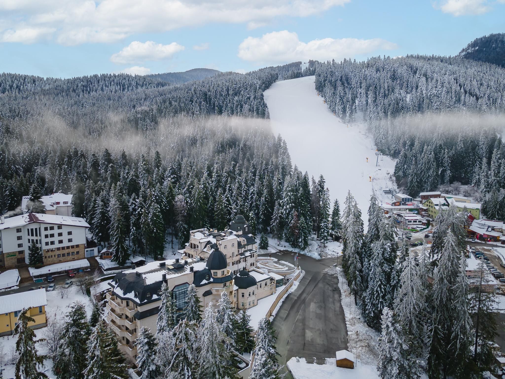 A snow-covered landscape with a river, buildings, and a forest.