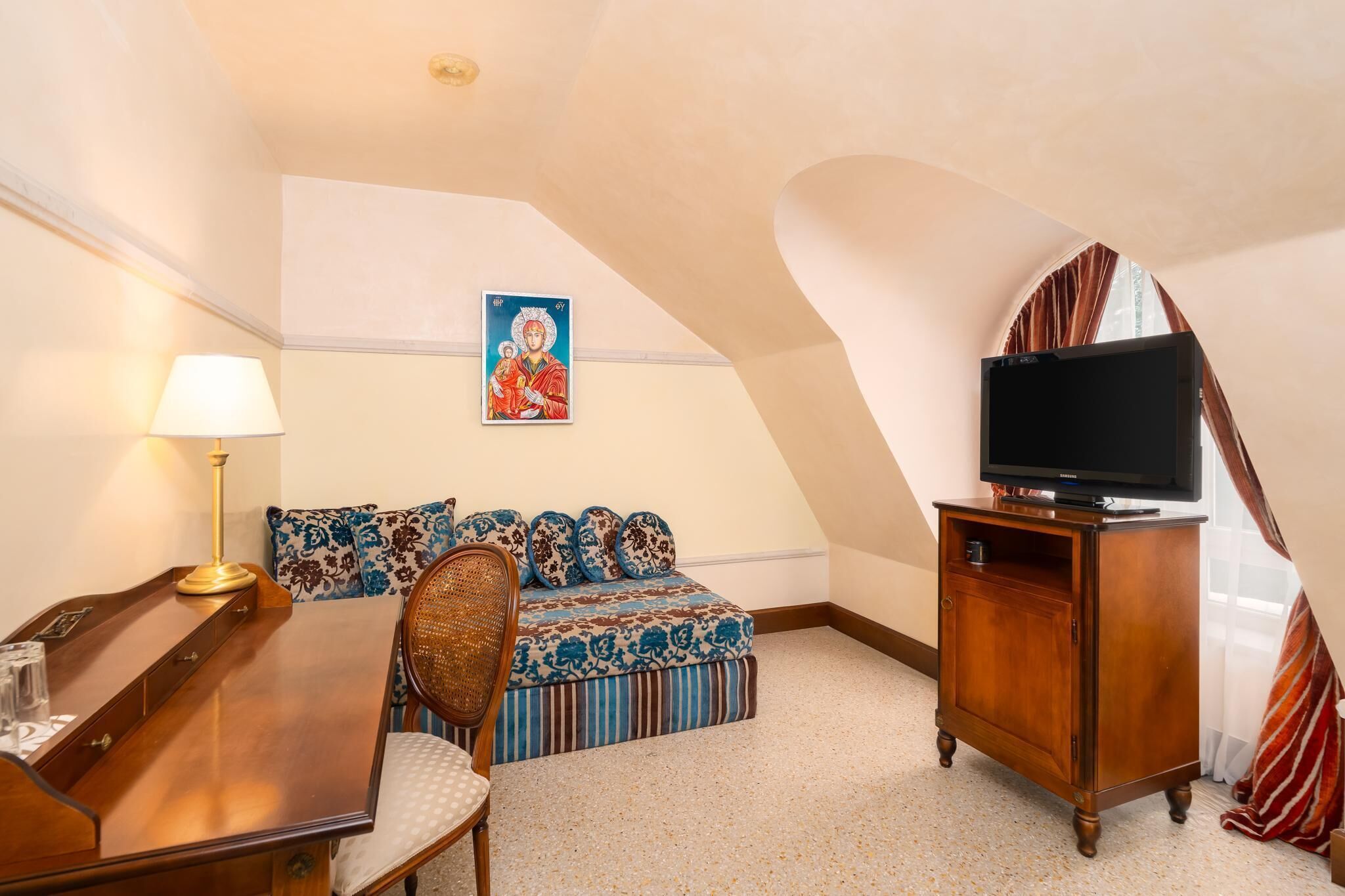 A cozy room with a wooden desk, a comfortable sofa, a television on a wooden cabinet, and a decorative painting on the wall.