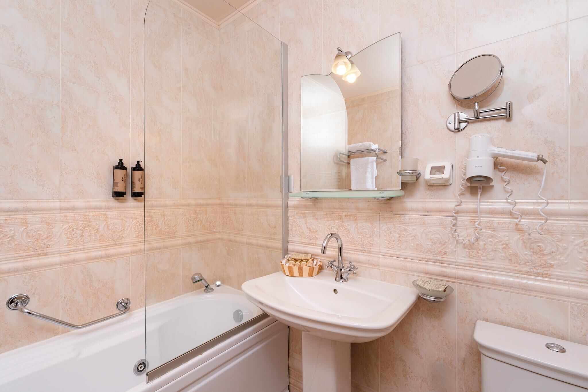A bathroom with a bathtub, sink, and toilet. There is a mirror, a towel rack, and a hairdryer on the wall.