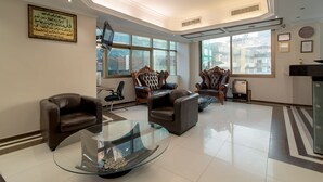 A spacious lobby with leather armchairs, a glass coffee table, and large windows offering views of the city.