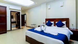 A hotel room with a large bed, a wooden headboard, a nightstand, and a vase with a single flower.