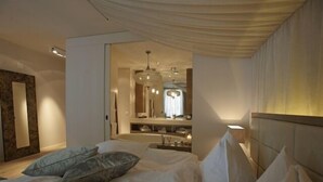 A modern hotel room with a large bed, a vanity with a mirror, and a chandelier. - Bad Bubendorf Hotel (Bubendorf)