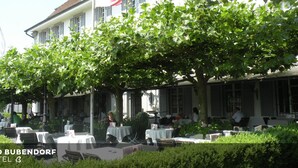 An outdoor seating area with tables and chairs, surrounded by greenery and a building with large windows. - Bad Bubendorf Hotel (Bubendorf)