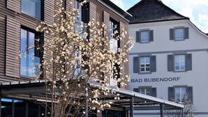 A building with a modern facade, a tree with white blossoms in front, and a sign reading "BAD BUBENDORF". - Bad Bubendorf Hotel (Bubendorf)