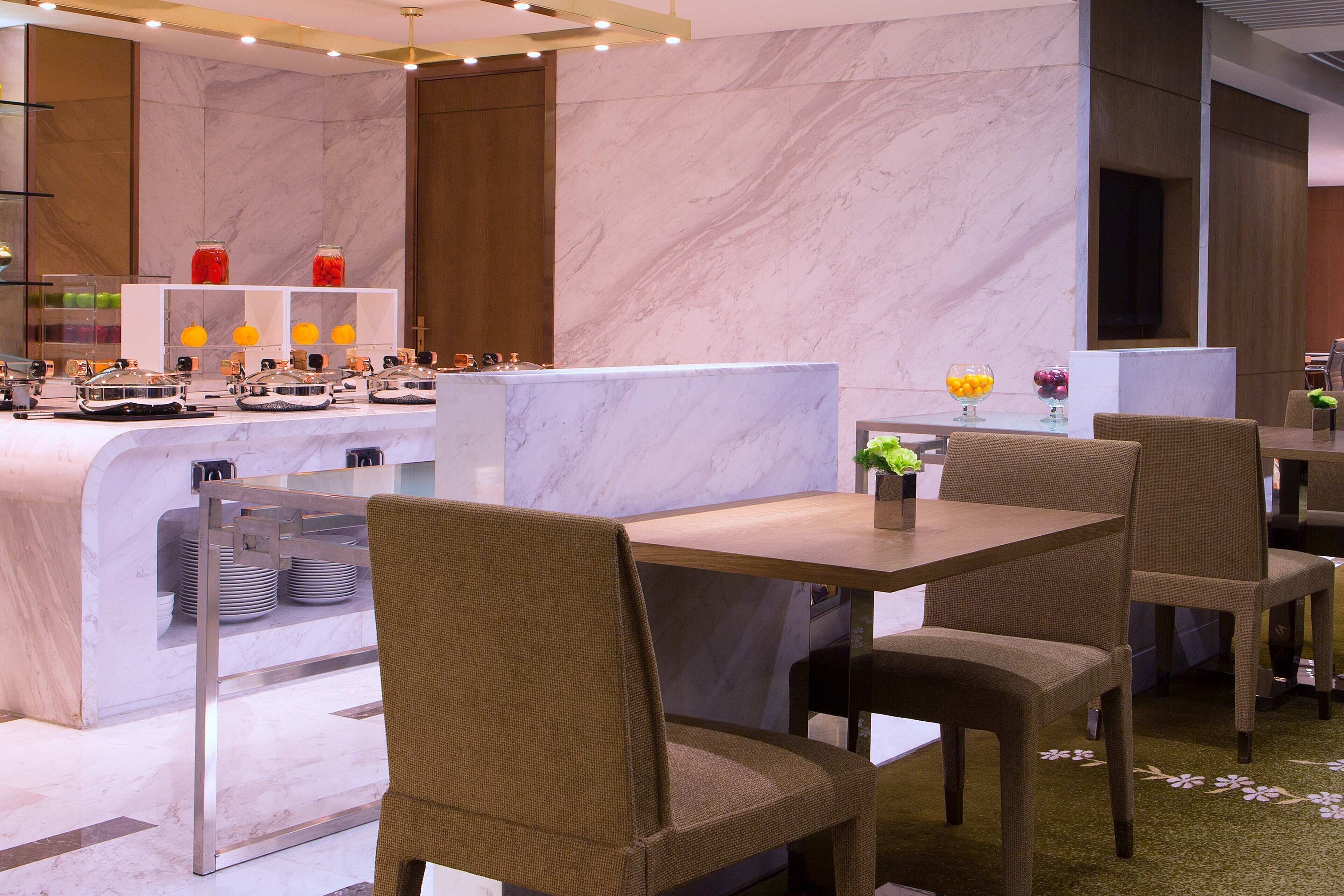 Un restaurant moderne avec des murs en marbre, un espace buffet, ainsi que des tables et des chaises en bois.