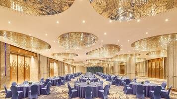A large banquet hall with round tables, blue chairs, and ornate chandeliers.