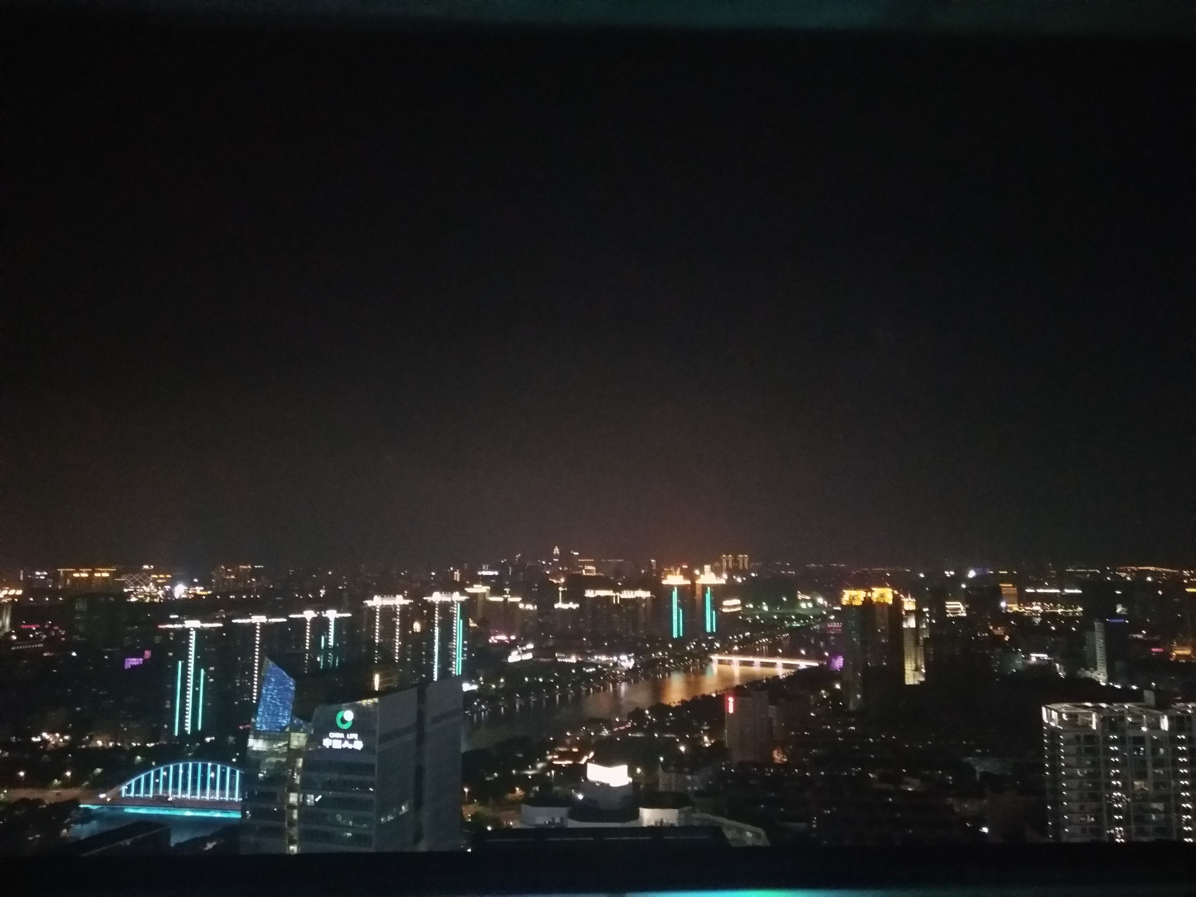 A nighttime cityscape with illuminated buildings and a bridge.