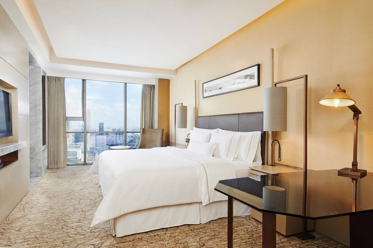 Une chambre d’hôtel avec un grand lit, un bureau, une lampe, une télévision et une vue sur la ville.