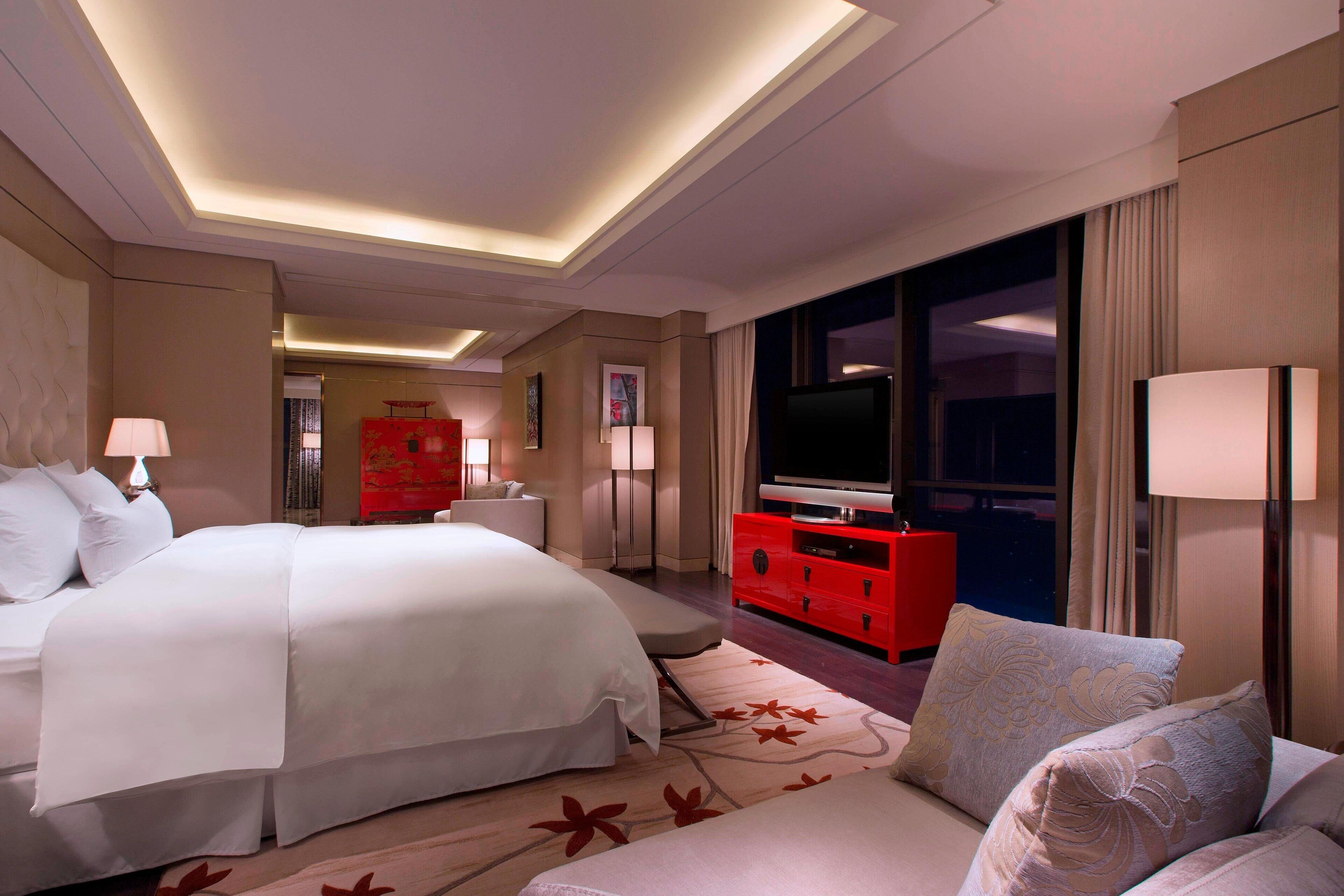 Una habitación de hotel con una cama grande, un aparador rojo, un televisor y un sofá.