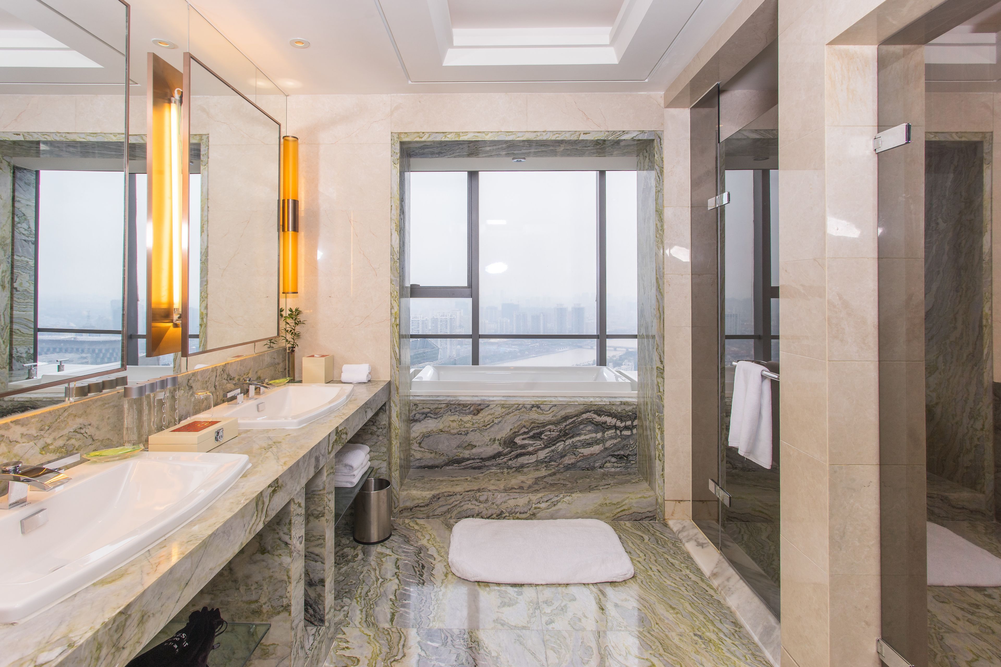 Ein modernes Badezimmer mit zwei Waschbecken, einer Badewanne und einem großen Fenster mit Blick auf die Stadt.