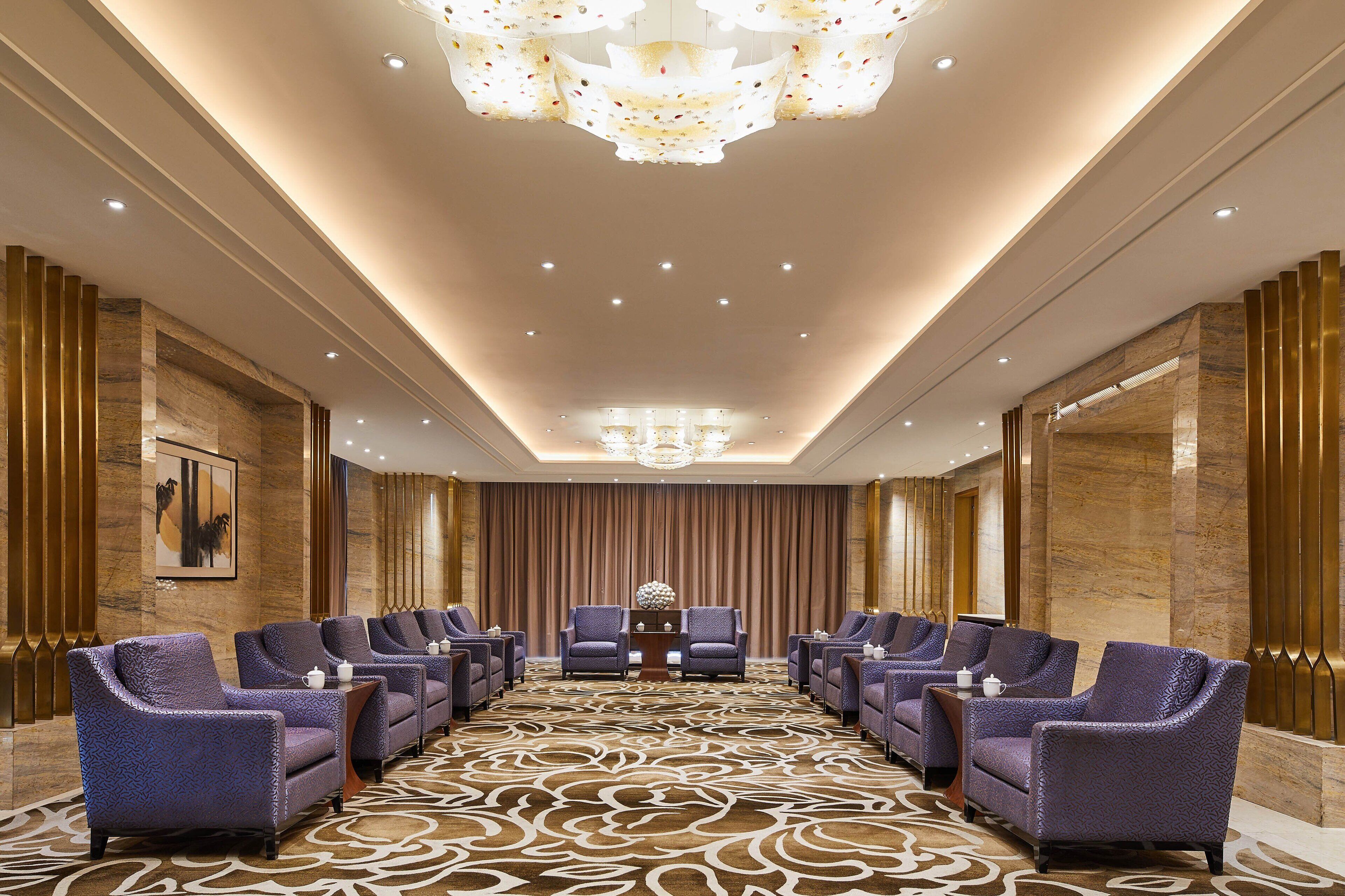 A conference room with a patterned carpet, rows of chairs, a chandelier, and a large painting on the wall.