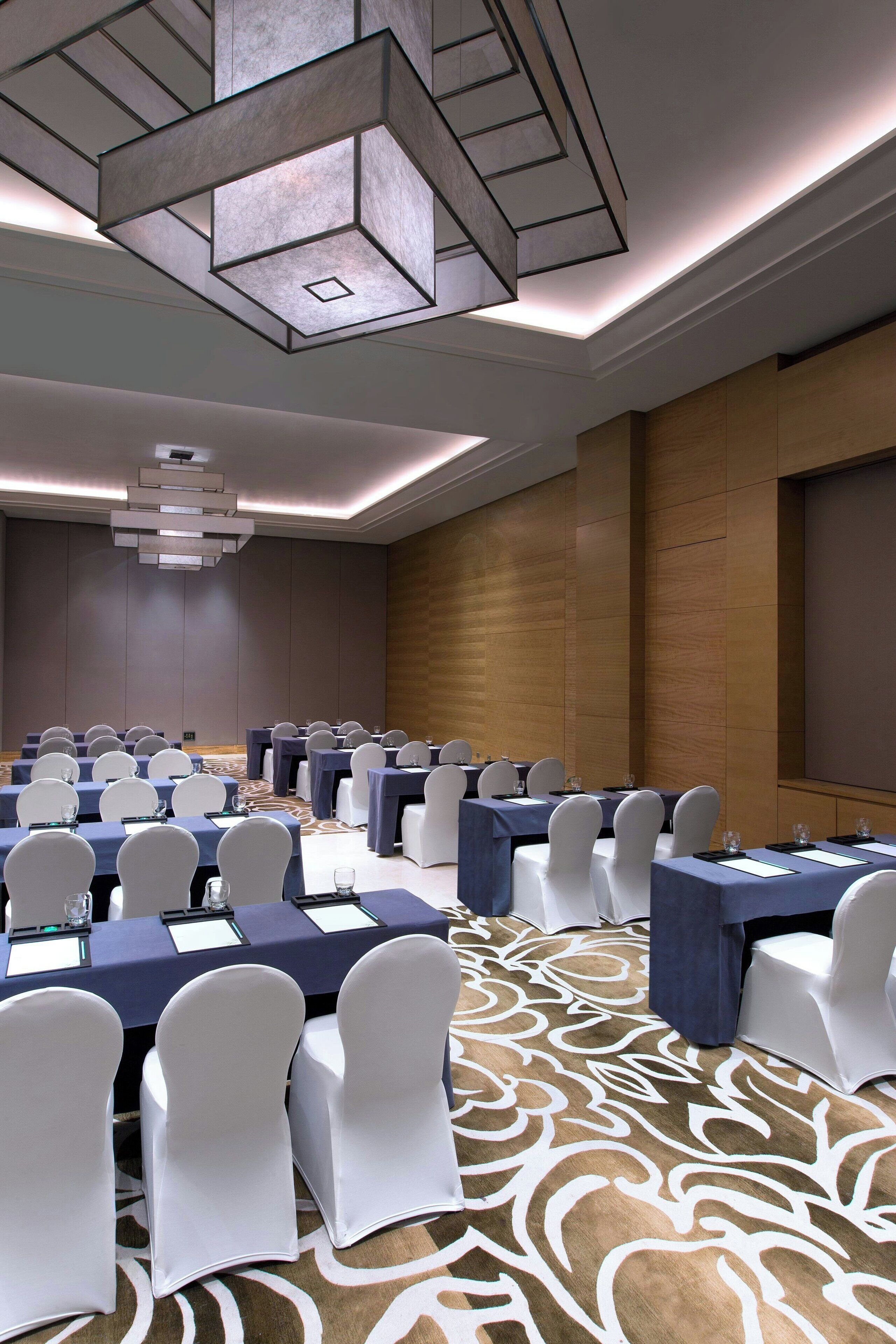 Un salón de conferencias con mesas dispuestas en filas, sillas blancas y una alfombra estampada.
