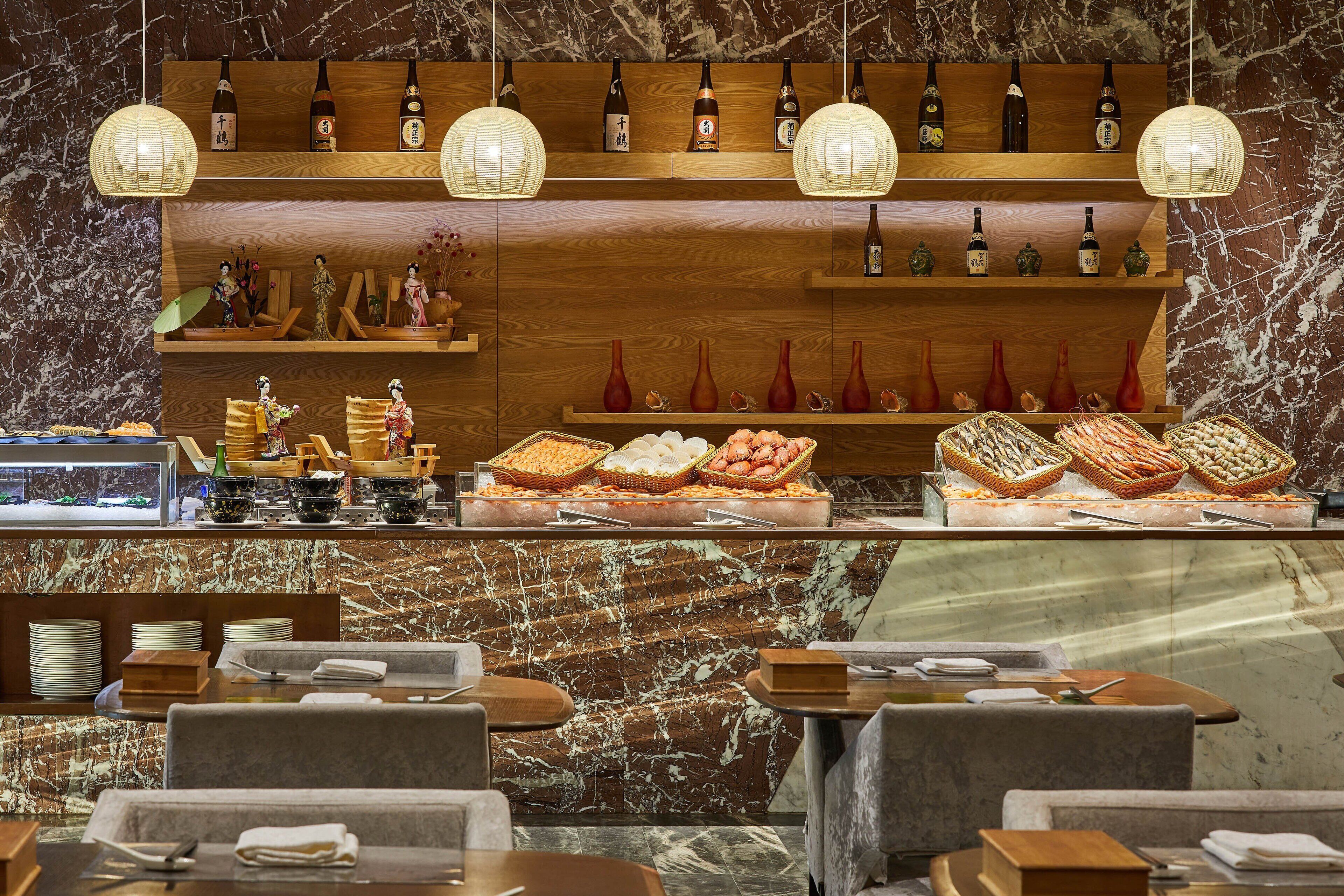 A restaurant with wooden shelves displaying bottles and vases, a buffet with seafood, and marble walls.