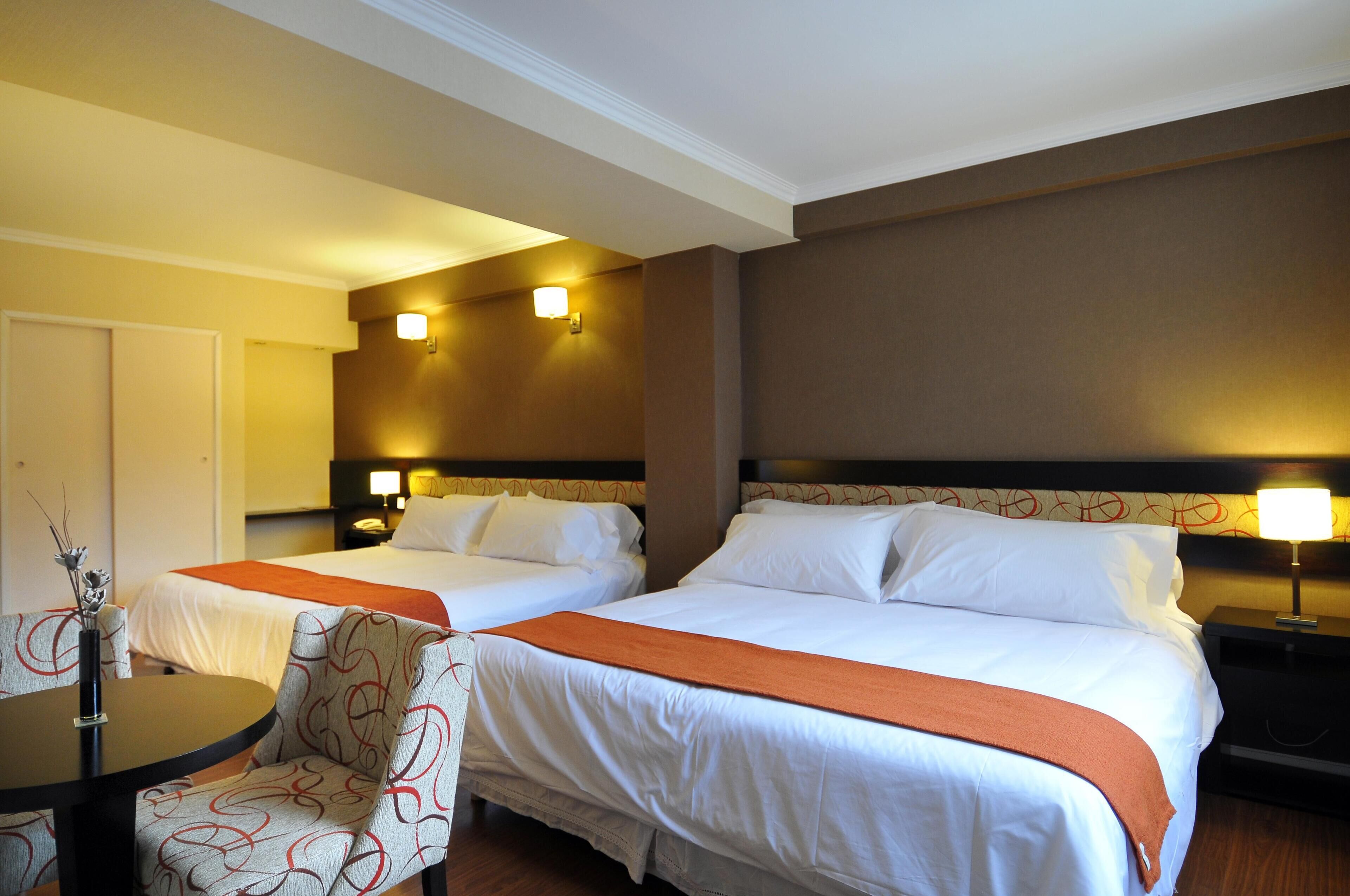 Habitación de hotel con dos camas, una mesa y una silla.