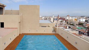 A rooftop pool with a wooden deck and a cityscape view. - Amerian Salta Hotel (Salta)