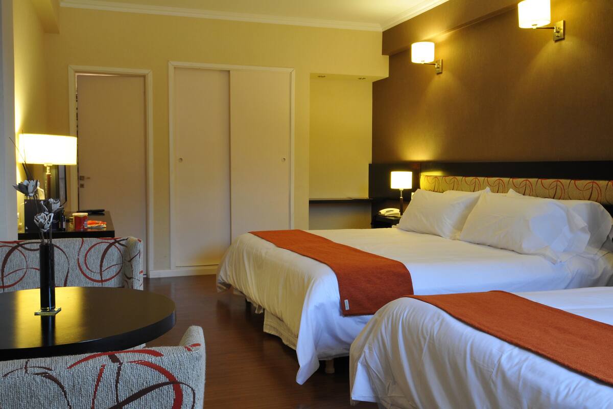 A hotel room with two beds, a round table, and a sofa.