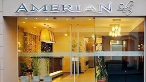 The entrance of the AMERIAN Hotel with a glass facade, interior lighting, and visible potted plants. - Amerian Salta Hotel (Salta)