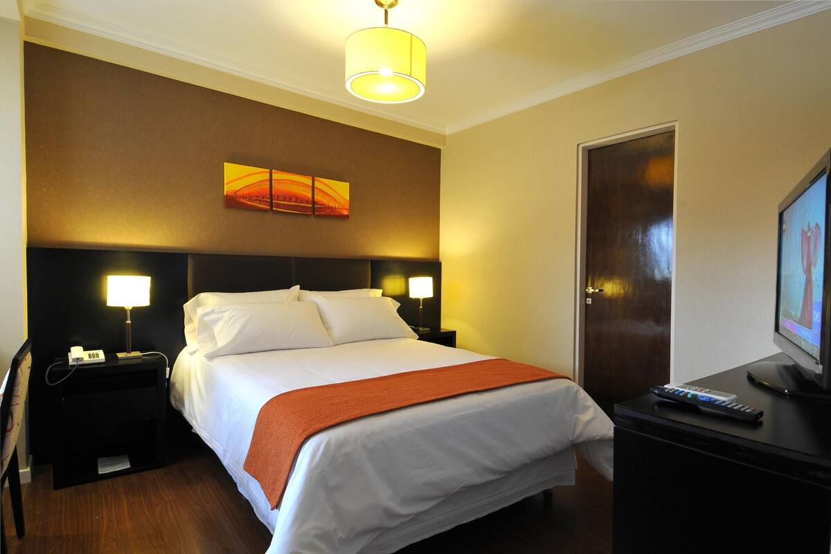 A hotel room with a bed, nightstands, a television, and a door.