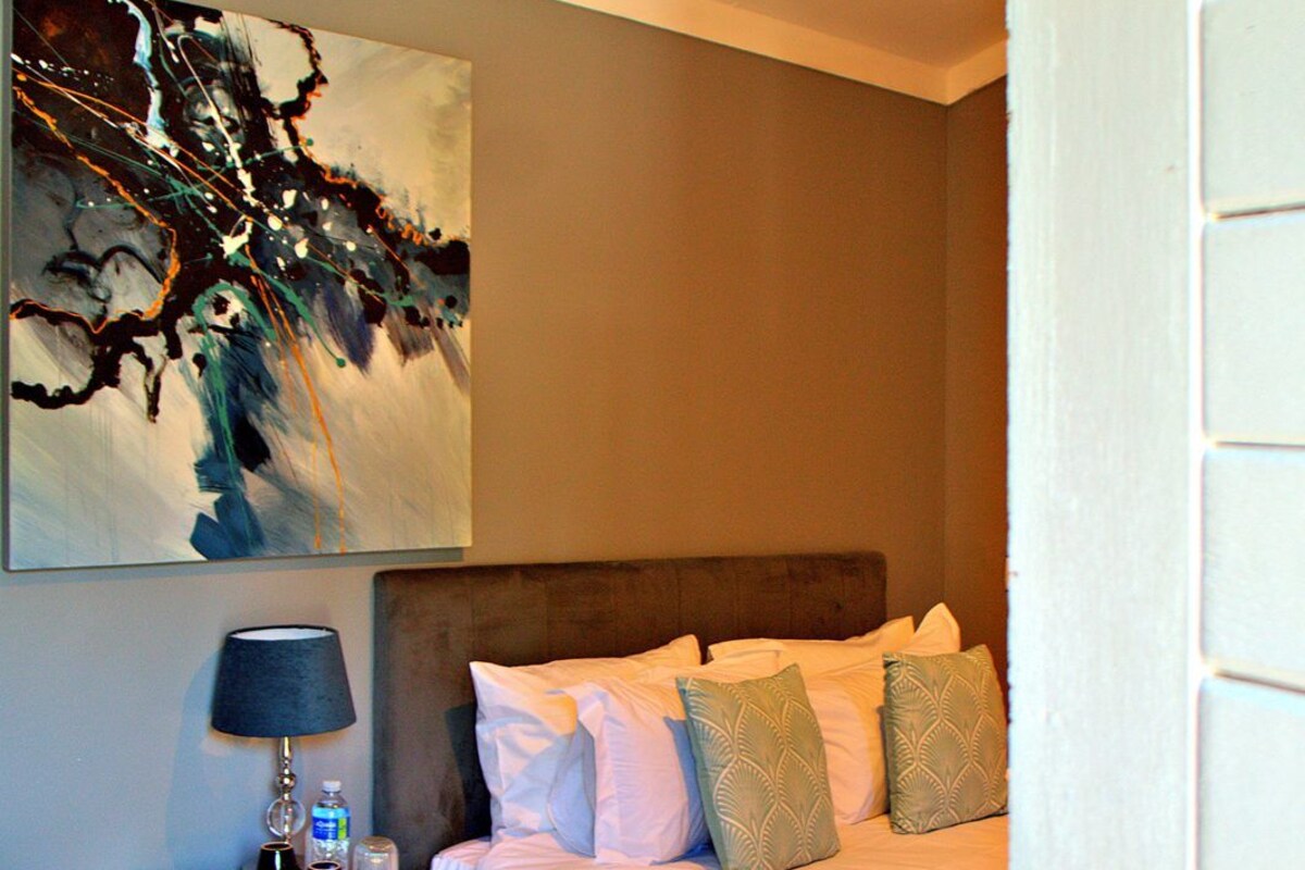 A bedroom with a bed, bedside table, lamp, and a painting on the wall.