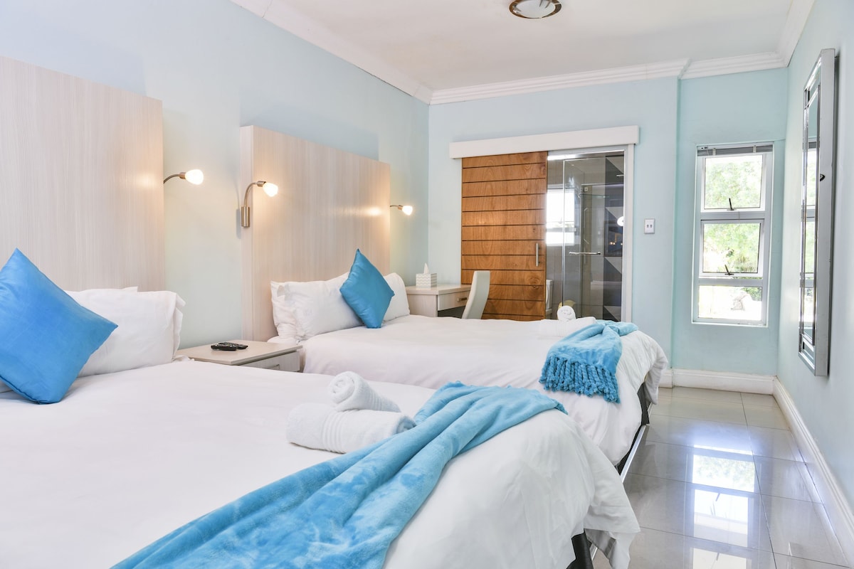 A hotel room with two beds, a wooden panel wall, a sliding glass door, and a large window.