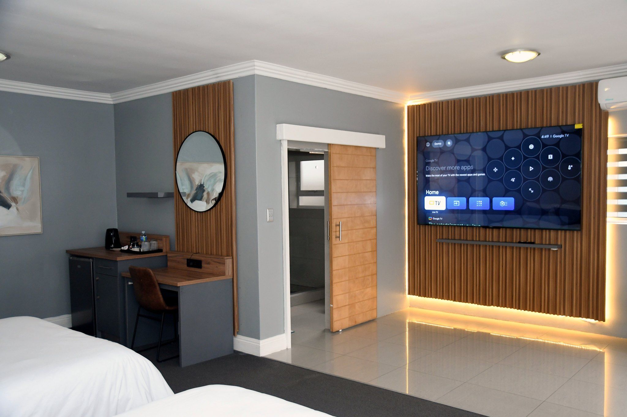 Quarto de hotel com cama, escrivaninha, espelho, televisão e parede de painéis de madeira.