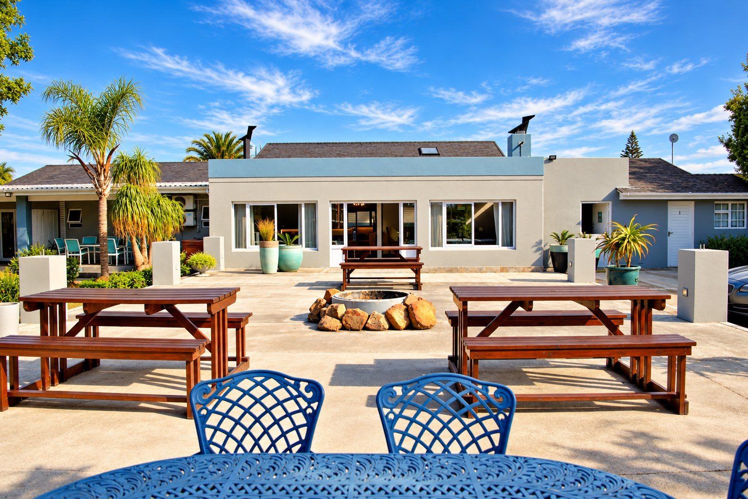 A patio area with wooden tables and chairs, a fire pit, and potted plants.