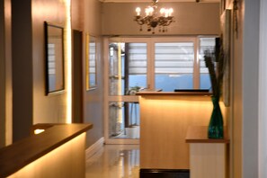 A hallway with a wooden reception desk, a green vase, and a chandelier.