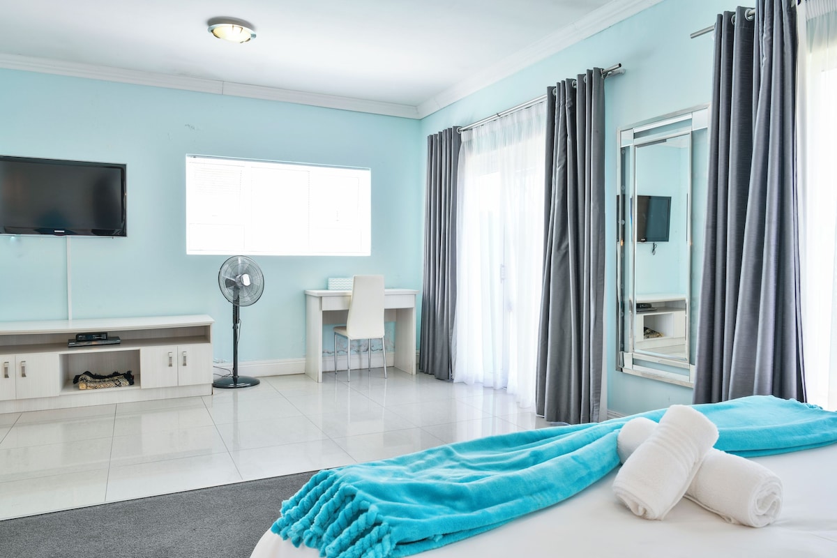 A hotel room with a bed, a desk, a chair, a TV, and a window with curtains.