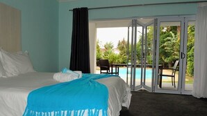 A bedroom with a bed, a blue throw blanket, a view of a pool and outdoor seating area through a glass door. - Al-Beit Lodge (Gqeberha (Port Elizabeth))