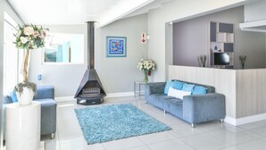 A modern living room with a grey sofa, a blue rug, a fireplace, and a TV on a wooden stand. - Al-Beit Lodge (Gqeberha (Port Elizabeth))