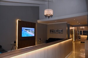 A hotel reception area with a TV, a chandelier, and a reception desk.