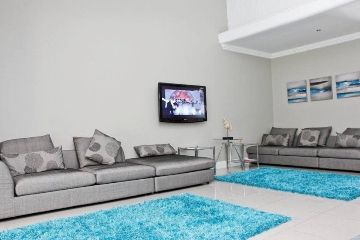 Ein modernes Wohnzimmer mit zwei grauen Sofas, einem Flachbildfernseher und blauen Teppichen.