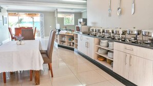 A modern kitchen with a dining area, featuring a buffet setup with multiple serving stations and a large table with chairs. - Al-Beit Lodge (Gqeberha (Port Elizabeth))