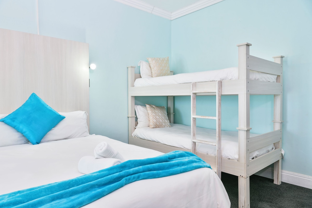 A room with a bunk bed and a single bed, both with white bedding and blue accents.