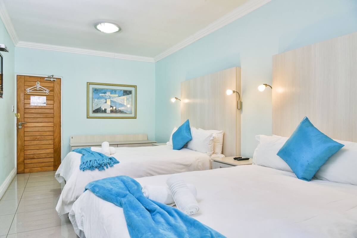 Ein Hotelzimmer mit zwei Betten, einer Holztür, einem gerahmten Bild und einer hellblauen Wand.