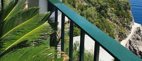 A balcony with a decorative head sculpture, a railing, and a view of the sea and cliffs.