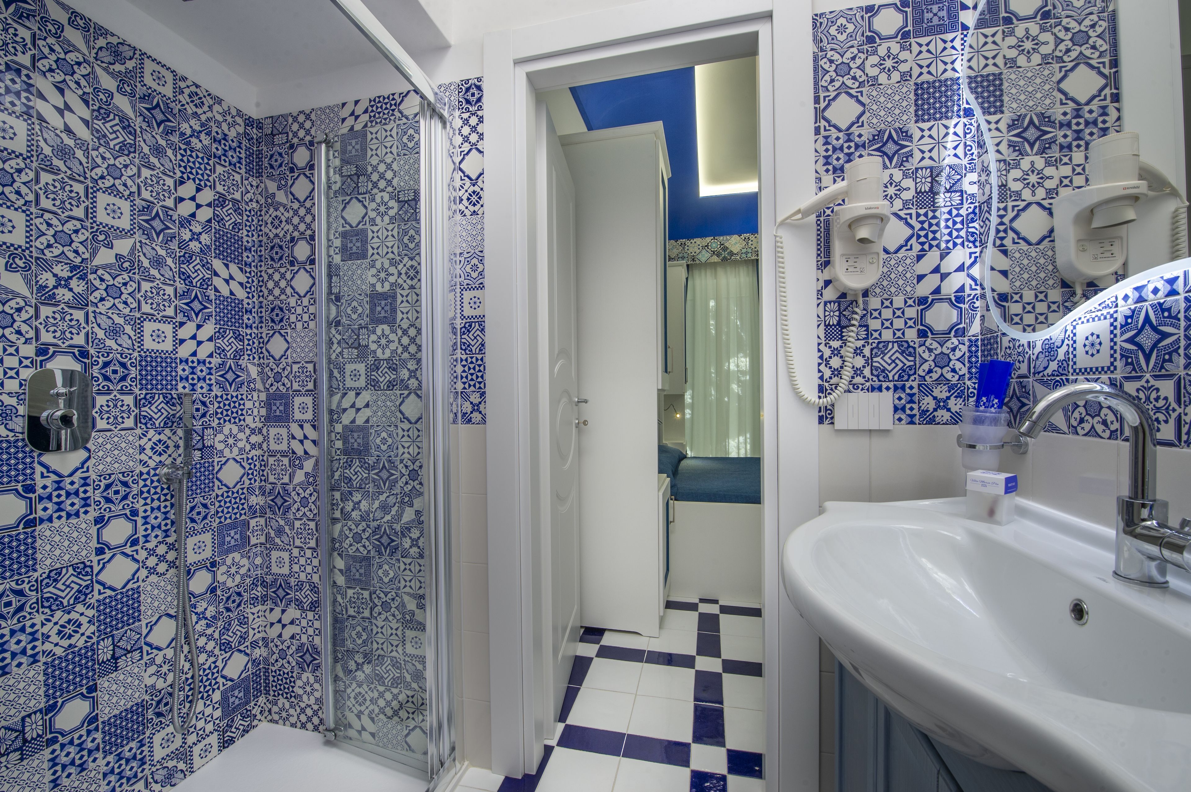 Un baño con azulejos blancos y azules estampados, un lavabo blanco y una zona de ducha.