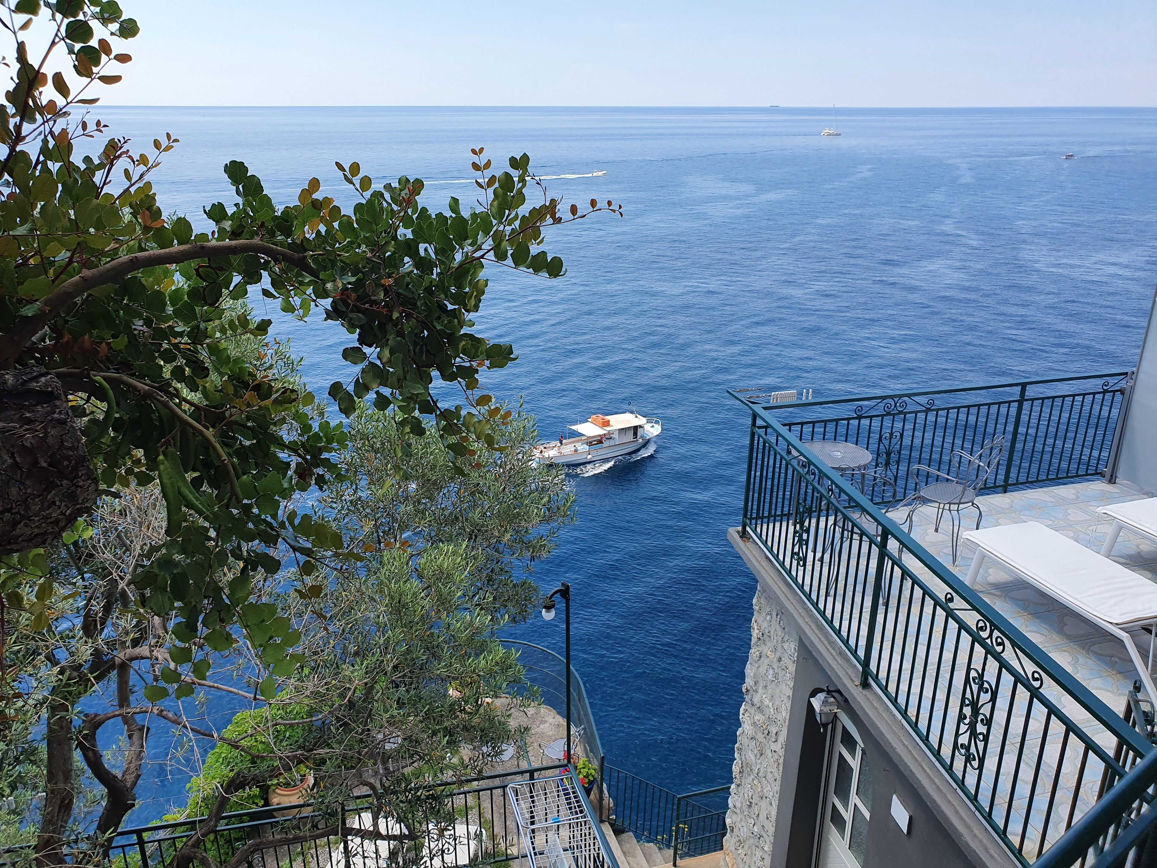 A balcony with a view of the sea, a boat, and a staircase leading down to the water.