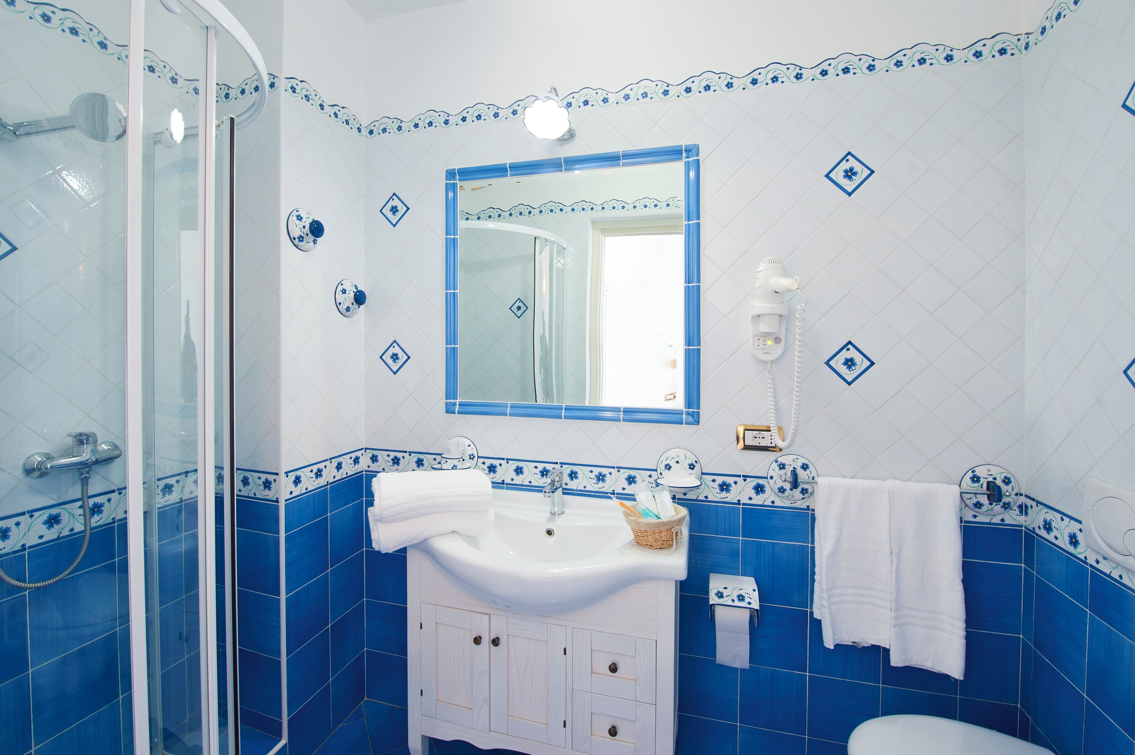 A bathroom with a glass shower enclosure, a sink with a mirror, and blue and white tiled walls.