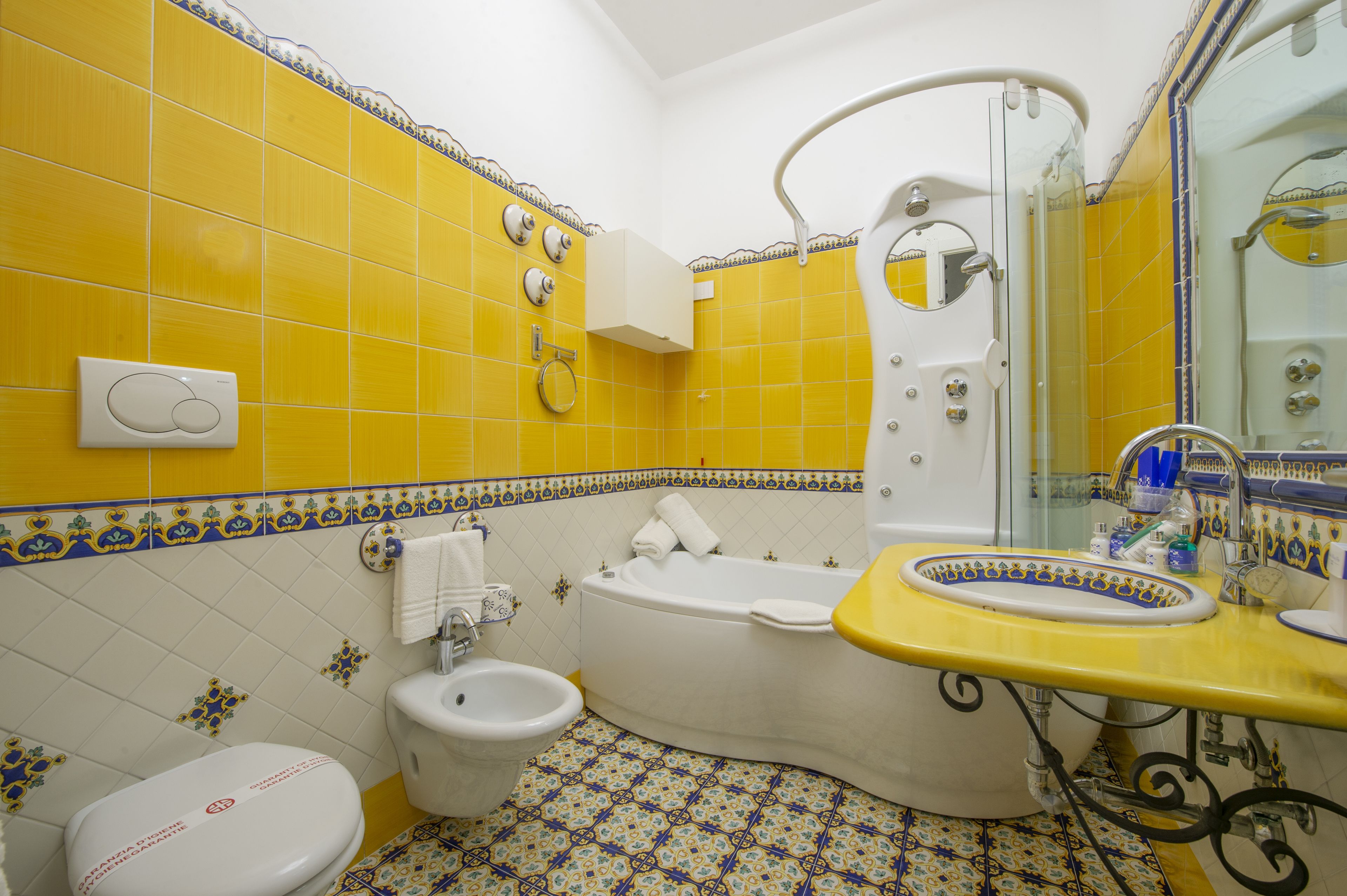 Un baño con paredes de azulejos amarillos, una bañera blanca, un lavamanos amarillo y un inodoro blanco.