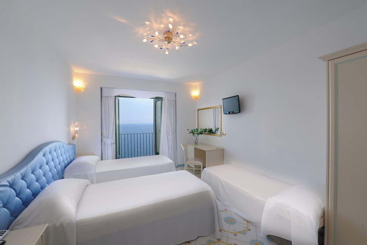 Une chambre d’hôtel avec deux lits, un bureau, une chaise, une télévision et un balcon avec vue.
