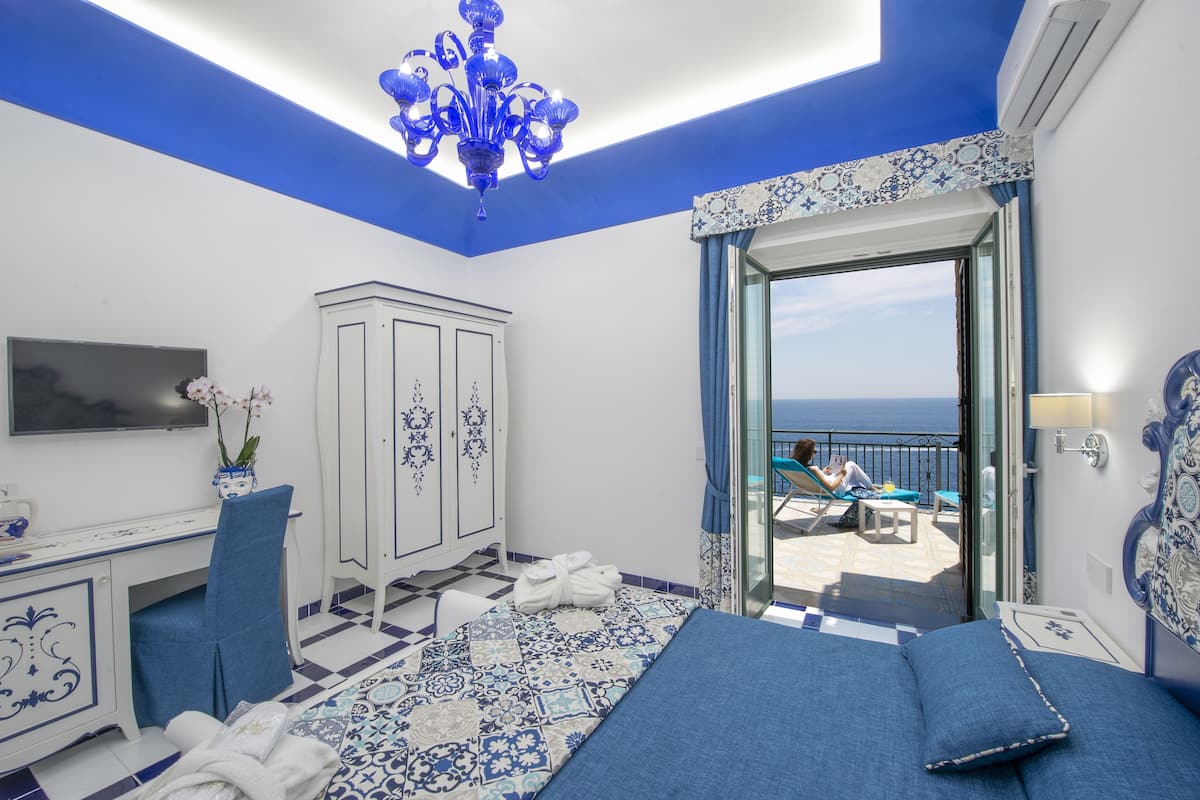Une chambre dotée d’un lit, d’un bureau et d’une armoire, et offrant un balcon avec vue sur la mer.