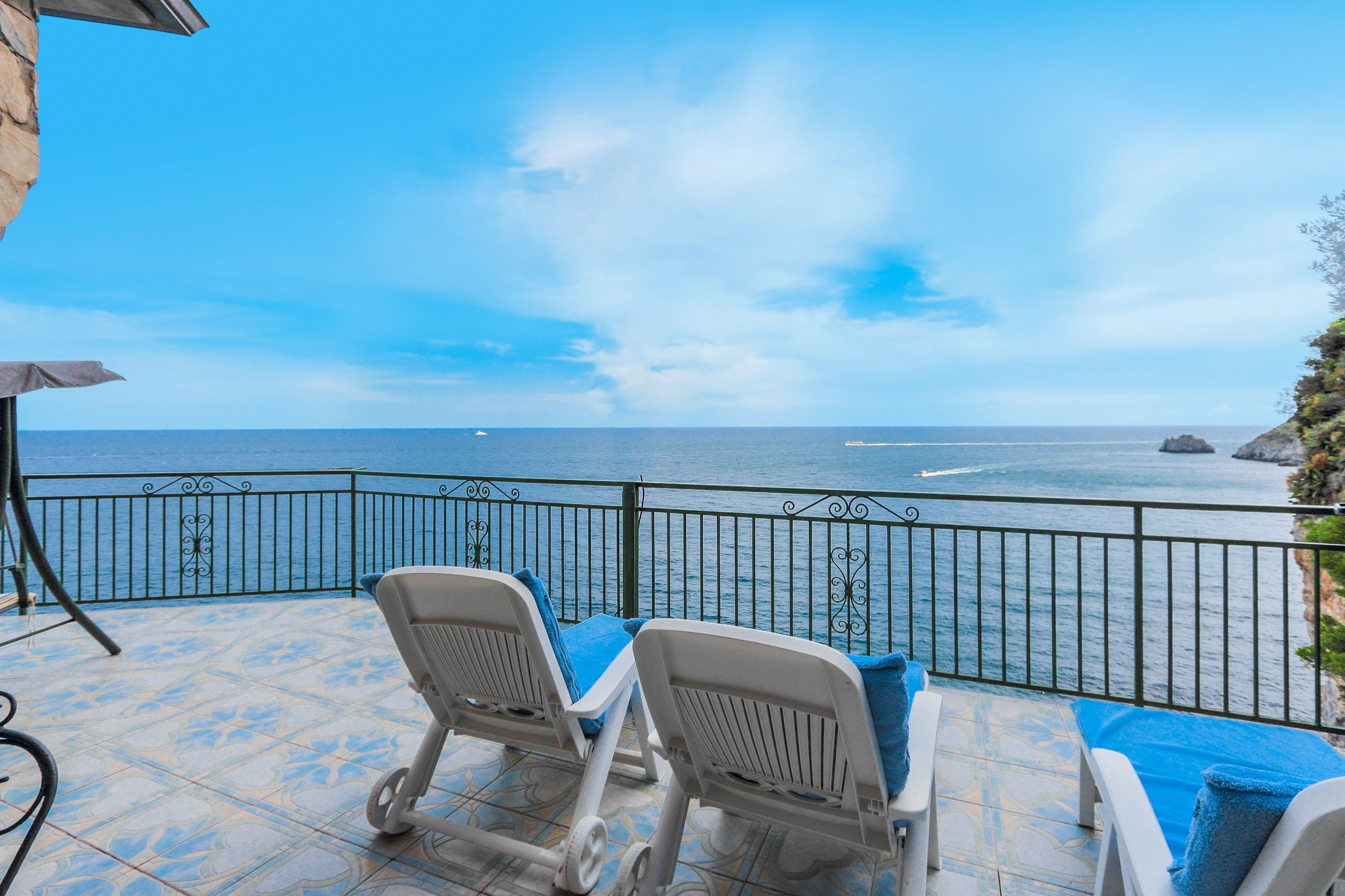Una terraza con dos sillones blancos y una mesa, con vista al mar y un cielo despejado.