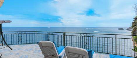 Una terraza con dos sillones blancos y una mesa, con vista al mar y un cielo despejado.